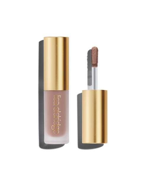A closed bottle of Lisa Eldridge Liquid Silk Liquid Eyeshadow in cool mauve shade Ione, with a gold cap containing an applicator wand with product on it, against a white background.